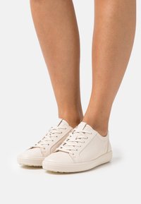 Baskets blanches à lacets en cuir lisse, avec un bout arrondi, des coutures minimalistes et des semelles en caoutchouc texturées pour une meilleure adhérence.