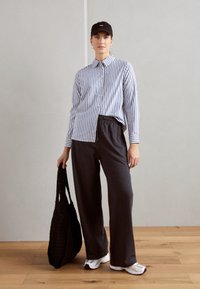Camicia a righe blu e bianche con bottoni, pantaloni scuri con coulisse, borsa a rete nera all'uncinetto e sneakers bianche. Design minimale.