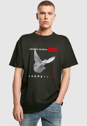 Sort bomulds t-shirt med et grafisk motiv af en due i flugt, med teksten "upscale studios SKY" og "ready to fly" i hvid og rød.