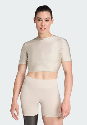 Bežasti sportski crop top i šorts izrađeni od glatkog, rastezljivog materijala. Ima jednostavan dizajn s suptilnim logotipom na lijevoj strani prsnog koša.
