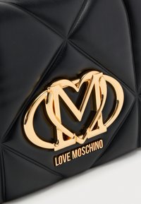 Μαύρη τσάντα από συνθετικό δέρμα με καπιτονέ σχέδιο, διακοσμημένη με λογότυπο σε χρυσό τόνο και ανάγλυφη λεπτομέρεια "LOVE MOSCHINO" στο κάτω μέρος. Λείο υφή με έντονες γραμμές.