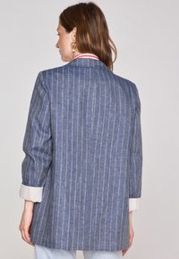Blazer bleu à rayures avec une coupe ajustée, présentant un détail de poignet blanc et une fente à l'arrière. Tissu léger avec une texture douce.