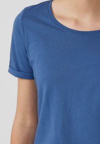 T-shirt bleu à manches courtes en tissu doux et léger. Il présente un col rond et des manches retroussées. Texture lisse sans motifs.