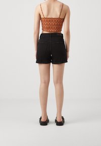 Pantalones cortos de mezclilla negra con dobladillos enrollados, combinados con un top corto y estampado con diseños ondulados en naranja y marrón. Calzado negro sencillo.