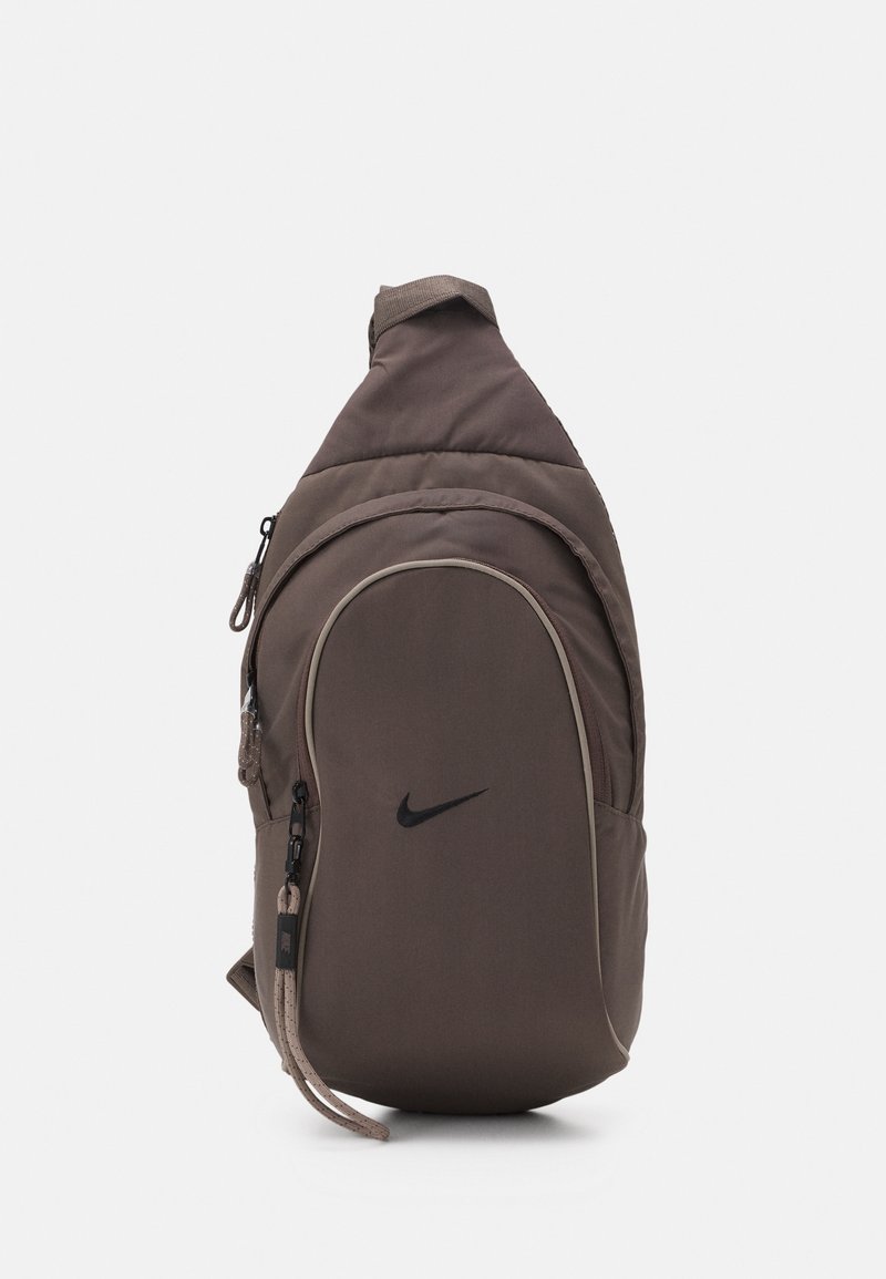 Hnědý nylonový krosničkový batoh s kulatým tvarem, zdobený černým logem Nike, zipovými kapsami a polstrovaným popruhem pro pohodlí.