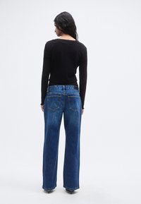 Μαύρο τοπ με μακριά μανίκια, ριμπ ύφασμα, τελείωμα με κυματιστό σχέδιο. Μπλε τζιν παντελόνι με φαρδύ πόδι, ξεθωριασμένο φινίρισμα, σχεδιασμός με πέντε τσέπες και εμφανείς λεπτομέρειες ραφής.