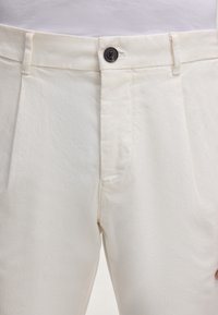 Katoenen blend broek, licht cremekleurig, met een enkele donkerknop, voorplooien en twee zijzakken. Gladde textuur, getailleerde pasvorm.