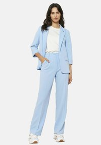 Svijetloplavi odijelo s krojenim sakoom s izrezanom reverom i širokim hlačama. Noseno preko bijele košulje, u kombinaciji s bijelim tenisicama.