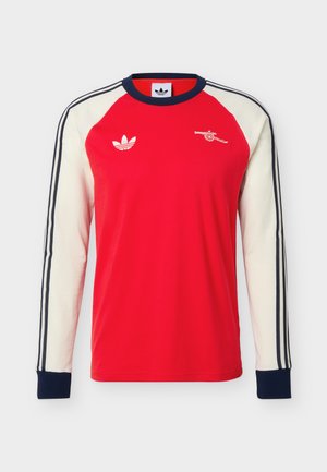 Red long-sleeve shirt with white sleeves, navy cuffs, three navy stripes on sleeves, Adidas logo on left chest, and a cannon logo on right chest.