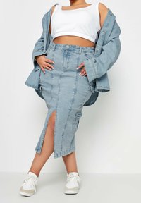 Ljust blå denimkjol med en framficka, hög midja och lapplådor, matchad med en vit kortärmad topp och en oversized denimjacka.