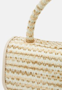 Woven handbag in cream and beige with textured surface, round shape, and a patterned handle; features gold accents and a smooth leather trim.