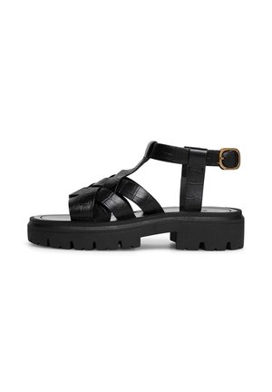 Černá kožená sandála s robustní vroubkovanou podrážkou, pletenými předními pásky, páskem kolem kotníku a zapínáním na sponu ve zlaté barvě na bílém pozadí.