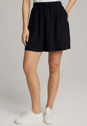 Ciemnoniebieska spódnica z elastycznym pasem, z regulowanym sznurkiem, miękka tkanina, boczne kieszenie i długość powyżej kolan, w zestawie z białymi sneakersami.