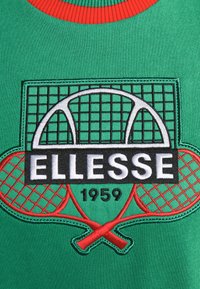 Tissu vert avec un col rouge comportant un motif brodé d'un filet de tennis, deux raquettes rouges croisées et le texte "ELLESSE 1959."