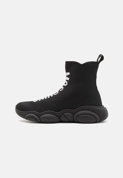 Black knitted ankle boots with a textured finish, featuring white lettering on the side and a chunky patterned sole. Pull tab at the back.