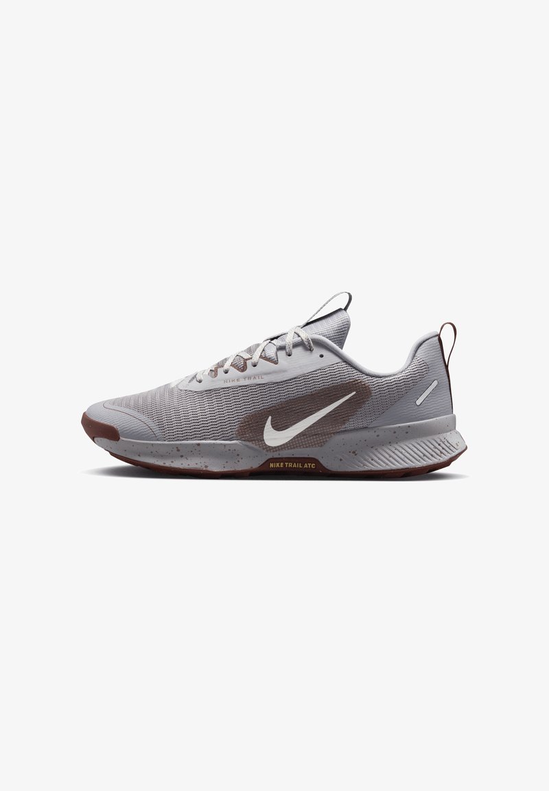 Chaussure de course sur sentier Nike grise et brune avec logo swoosh blanc, tige en tricot texturé, lacets et semelle mouchetée, vue de côté sur fond blanc.