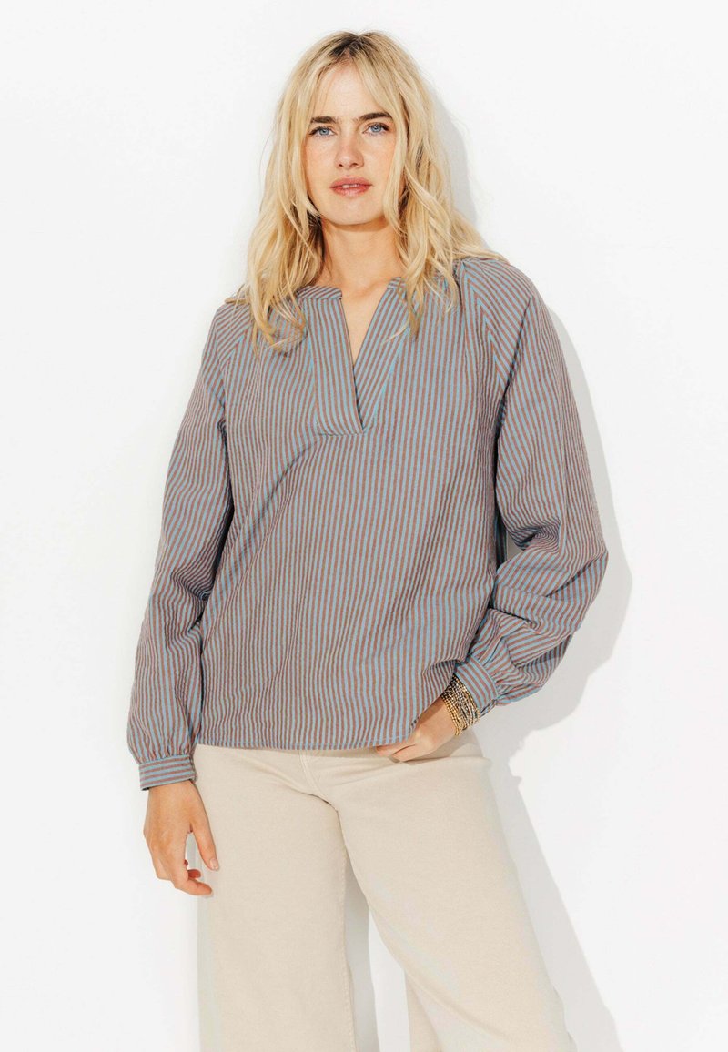 Pull-over rayé avec un col en V, des manches longues et une coupe décontractée. Les couleurs incluent des rayures beige, bleues et brunes. Tissu texturé.