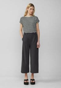 Haut rayé noir et blanc associé à un pantalon taille haute gris avec des boutons à l'avant et des sandales à plateforme noires et épaisses.