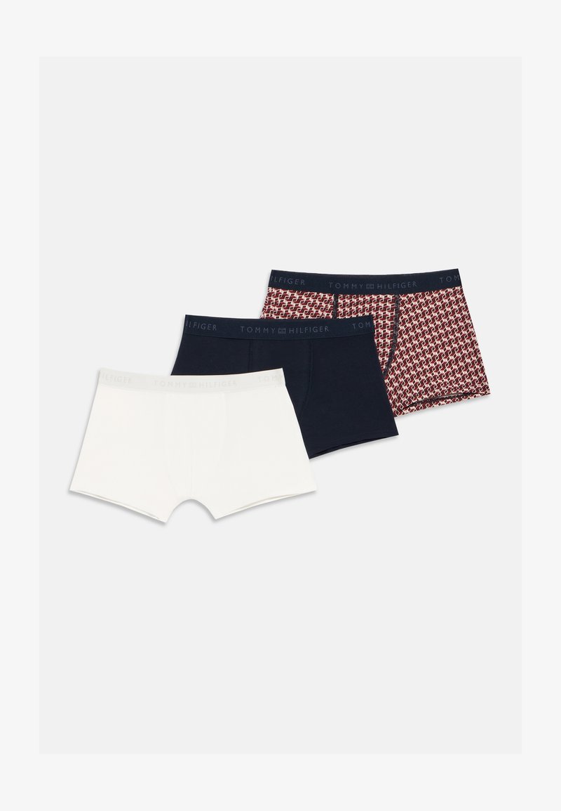 Tri moške spodnje boksarice v beli, enobarvni mornarsko modri in rdeči z vzorcem, vsake s pasom z logotipom Tommy Hilfiger, položene na ravni beli podlagi.