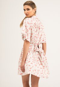 Kwiatowa sukienka z lekkiego materiału o białym tle i różowo-zielonym wzorze, z krótkimi rękawami i szczegółem w postaci wiązania w talii.