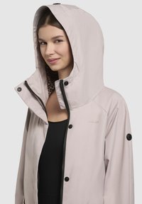 Veste imperméable rose clair avec capuche, dotée d'une doublure à imprimé léopard et d'accents en métal noir. Texture lisse, fermetures éclair et à bouton-pression.