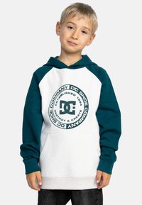 Sudadera con capucha de mangas azul verdosas y cuerpo blanco, que presenta un logo gráfico circular centrado en la parte frontal. El material parece suave y texturizado.