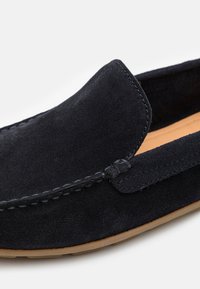 Marineblaue Wildleder-Slipper mit glatter Textur, runder Zehenform und kontrastierenden Nähten. Die Sohle aus Naturkautschuk sorgt für Langlebigkeit.