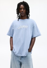 Light blue oversized t-shirt with short sleeves, featuring "Atlanta Georgia" in white cursive embroidery across the chest.