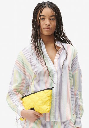Gestreifte, pastellfarbene Hemdbluse mit entspannter Passform, die ein gelbes, gesteppte Täschchen mit schwarzem Reißverschlussdetail hält.
