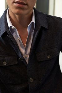 Tengerészkék gyapjú zakó két mellzsebbel, gombos rögz�ítéssel, alatta világoskék ing, amelynek a gallérja szabadon áll és gombos díszítése van.