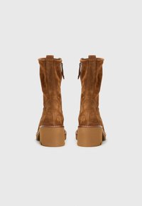 Bottines en suède marron avec une texture lisse, présentant un bout arrondi, des talons épais et des fermetures éclair à l'arrière pour un enfilage facile.