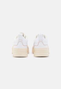 Sneakers bianchi con una suola color crema testurizzata e una leggera fodera in tessuto, caratterizzati da un design pulito e dettagli di cucitura minimi.