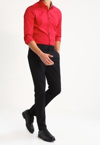 Rode button-up overhemd met lange mouwen, zwarte broek en zwarte nette schoenen. Het overhemd heeft een kraag en knopen; de broek is slim-fit.