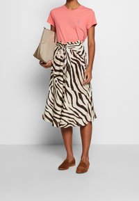 Pink short-sleeve t-shirt, beige zebra-print midi skirt with a tie waist, brown suede loafers, and a beige handbag.