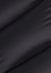 Schwarzer, glatter Stoff mit glänzender Textur, der diagonale, gesteppte Muster und subtile Details entlang der Nähte aufweist.