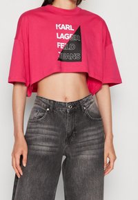 Růžové zkrácené tričko s černým grafickým textem "KARL LAGERFELD JEANS" na přední straně. Nosené s tmavě šedými džínami s vysokým pasem.