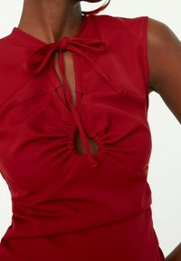 Rode mouwloze top met een geplooid ontwerp, voorzien van een keyhole uitsnijding bij de borst en een strikdetails bij de hals. Zachte stofstructuur.