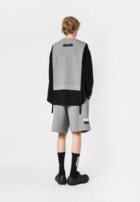 Sudadera gris con mangas negras, combinada con pantalones cortos grises. Presenta una etiqueta en la sudadera y zapatos negros de slip-on. Calcetines negros con texto blanco.