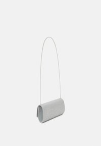 Pieni hopeinen kimalteleva clutch-laukku, jossa on kaarevat reunat ja ohut hopeaketjuhihna, valkoista taustaa vasten.
