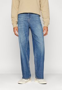 Jean en denim bleu clair à coupe décontractée, doté d'une jambe droite, d'un effet froissé subtil et de détails cousus le long des coutures.