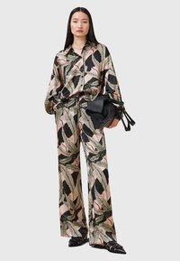 Camicia di seta stampata e pantaloni abbinati con motivo foglia tropicale su sfondo nero. L'outfit ha una vestibilità ampia e gambe larghe.