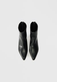 Bottines en cuir noir avec un bout pointu et une texture lisse. Présentent une tige basse et une tirette à l'arrière pour un enfilage facile.