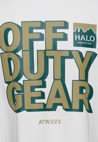 Napis „OFF DUTY GEAR” dużymi zielonymi i beżowymi literami na białym materiale z małym logo „HALO 196819721981” i napisem „ATW 223” poniżej.