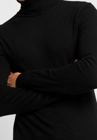 Svart polotröja gjord av stickat material. Fitted design med långa ärmar och ribbade ärmslut. Slät textur utan synliga mönster eller accenter.