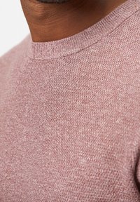 Jasnoróżowy sweter z dzianiny z okrągłym dekoltem. Tekstura wydaje się miękka i lekko fakturowana, ukazując gładki, ale złożony wzór.