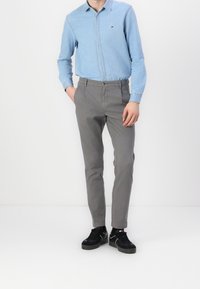 Světle modrá džínová košile s knoflíkovým zapínáním; šedé zúžené kalhoty; černé tenisky; na košili je malé logo.