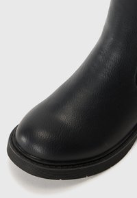 Svarte skinnankleboots med rund tå, teksturert overflate og gummisåle med horisontale spor for bedre grep.