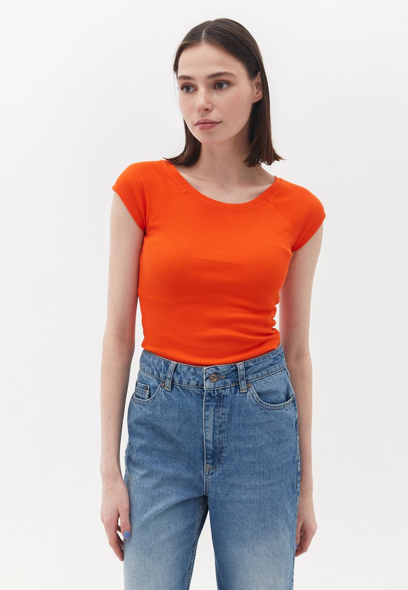 Top naranja de manga corta con canalé, combinado con jeans de mezclilla azules de cintura alta. El top presenta un escote redondo y una silueta ajustada.