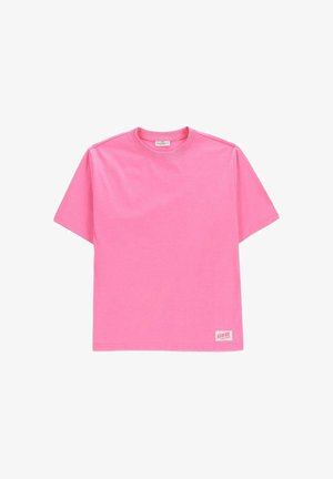 Gładki, jasnoróżowy T-shirt z krótkim rękawem, okrągłym dekoltem i małą prostokątną metką "HAWAII" w pobliżu dolnego brzegu z przodu po prawej stronie.