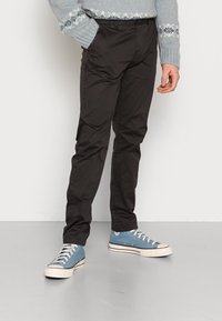Černé slim-fit kalhoty s hladkou texturou a bočními kapsami, doplněné světle modrými plátěnými teniskami s bílými gumovými podrážkami.